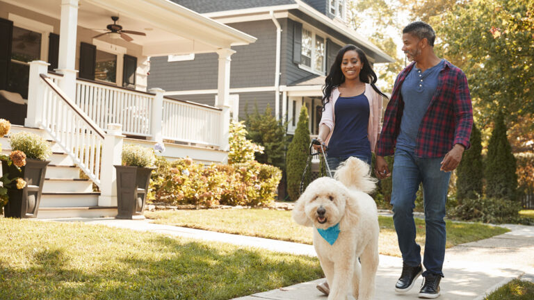 man and woman walking their white dog on sidewalk